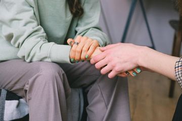 A woman is holding another woman 's hand while sitting in a chair.