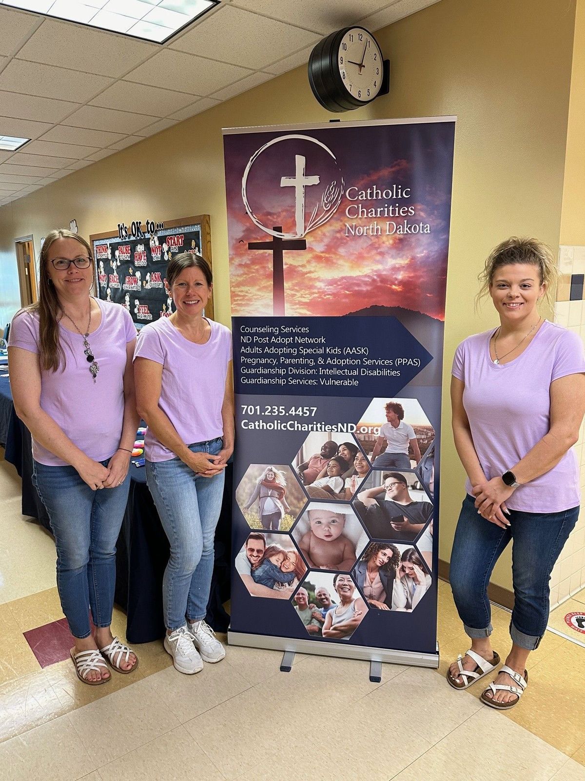 Three women are standing in front of a banner with a cross on it.