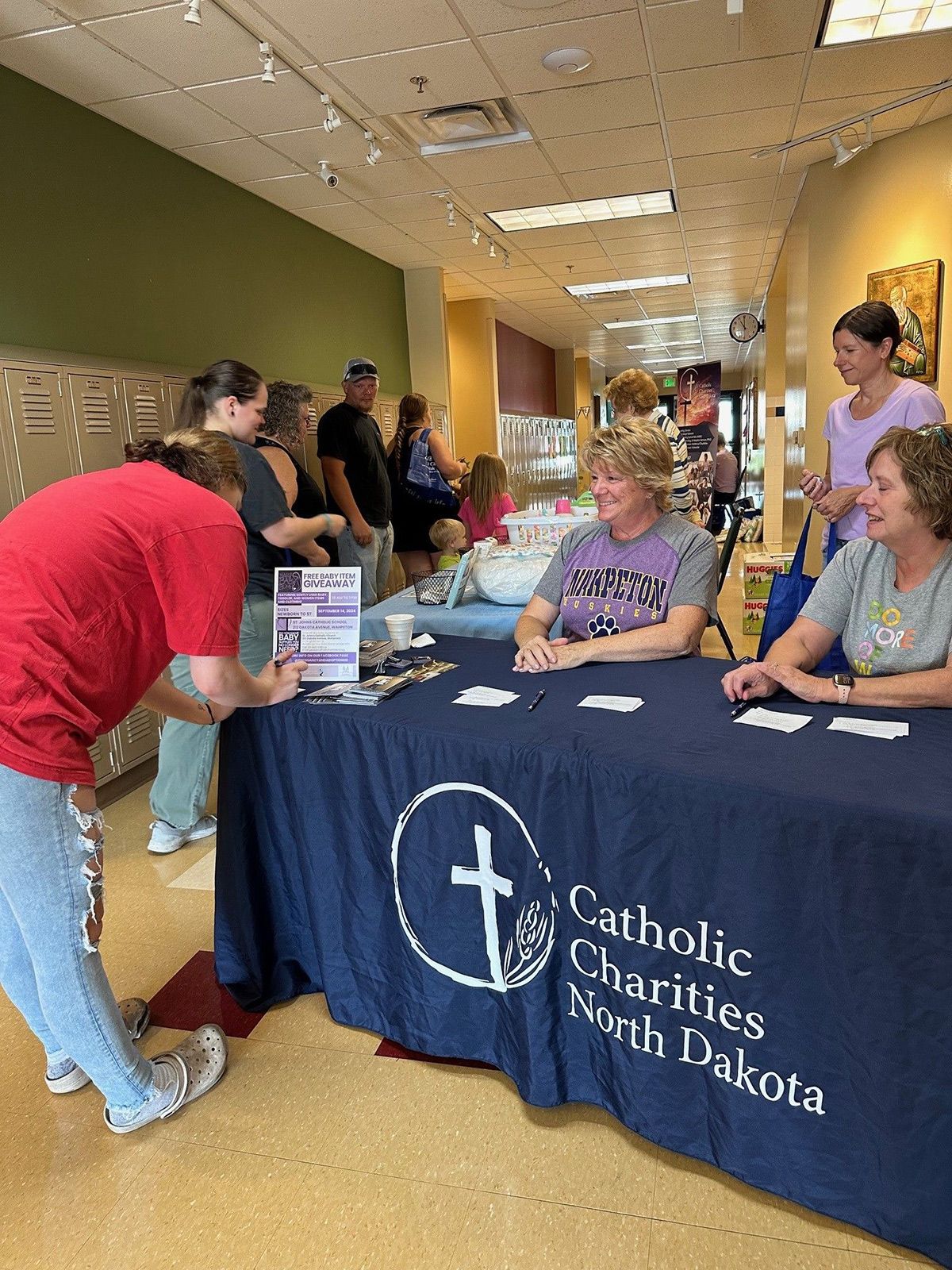 A group of people are sitting at a table with a blue table cloth that says Catholic Charities North Dakota