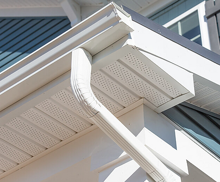 White house eaves with decorative gutter and soffit against gray siding and windows