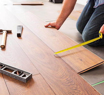 Person measuring a wooden floor plank with a tape measure during installation