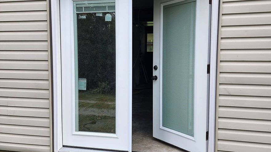 Open patio doors at a house exterior, with one glass door partially open and beige siding visible.