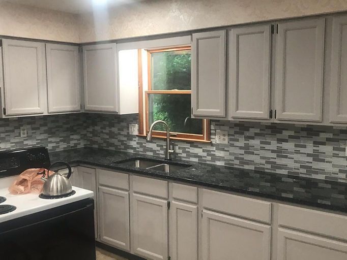 Kitchen with white cabinets, gray mosaic backsplash, black countertop, and a window above the sink.