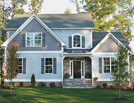 Two-story gray house with white trim, front porch, and landscaped lawn among trees