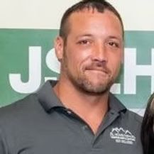 Man in a gray polo shirt standing before a green sign, slight smile.