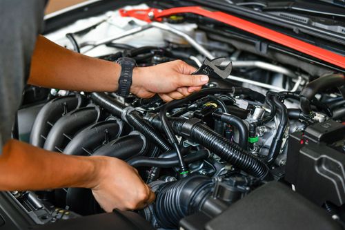 Mechanic using tools to work on a car engine under the hood.