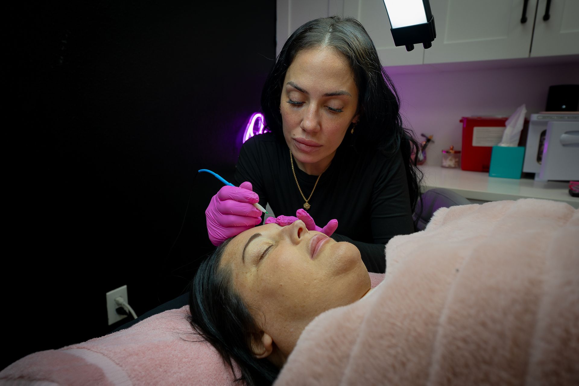 A woman is laying on a bed getting a tattoo on her face.
