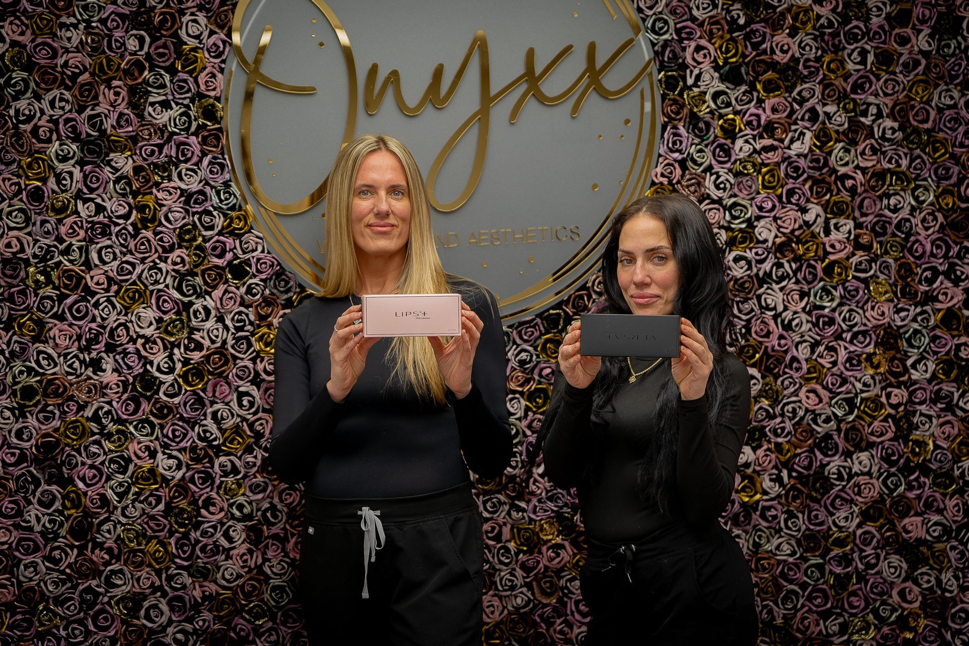 Two women are standing next to each other holding cards in front of a floral wall.