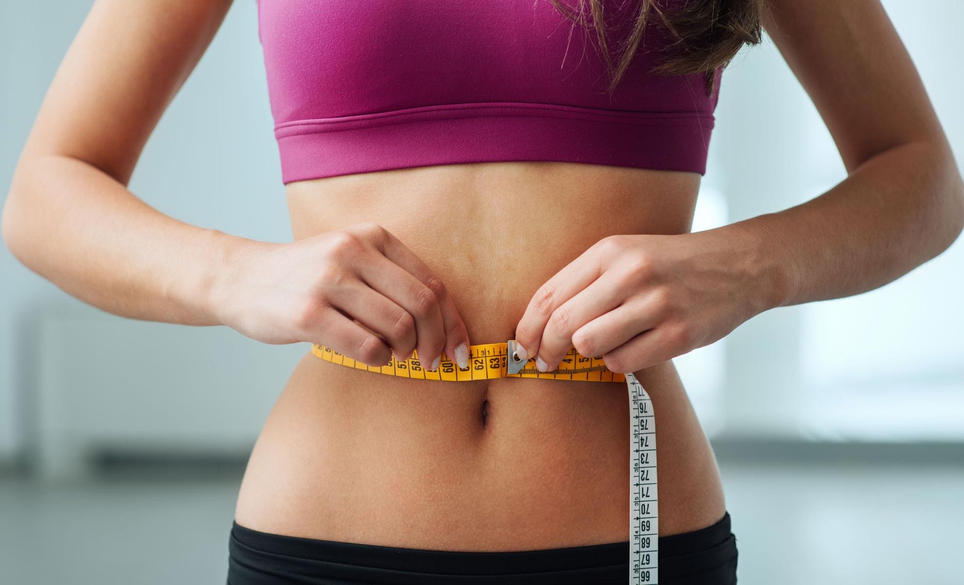 A woman is measuring her waist with a tape measure.