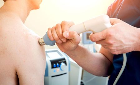 A man is getting a physical therapy treatment on his shoulder.