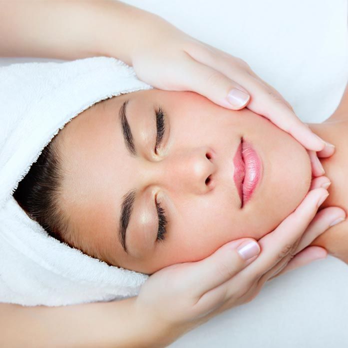 A woman with a towel wrapped around her head is getting a facial massage