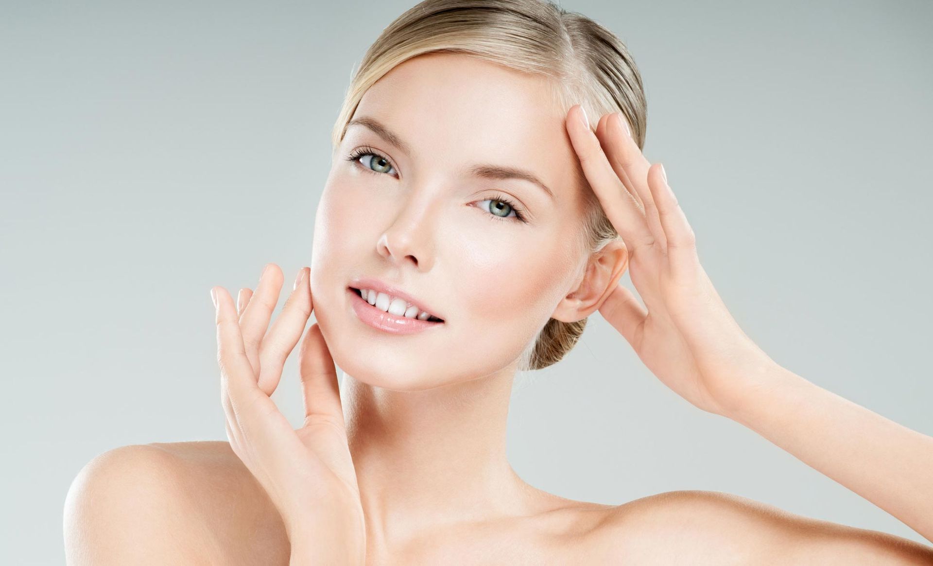 A woman is touching her face with her hands and smiling.
