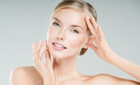 A woman is touching her face with her hands and smiling.