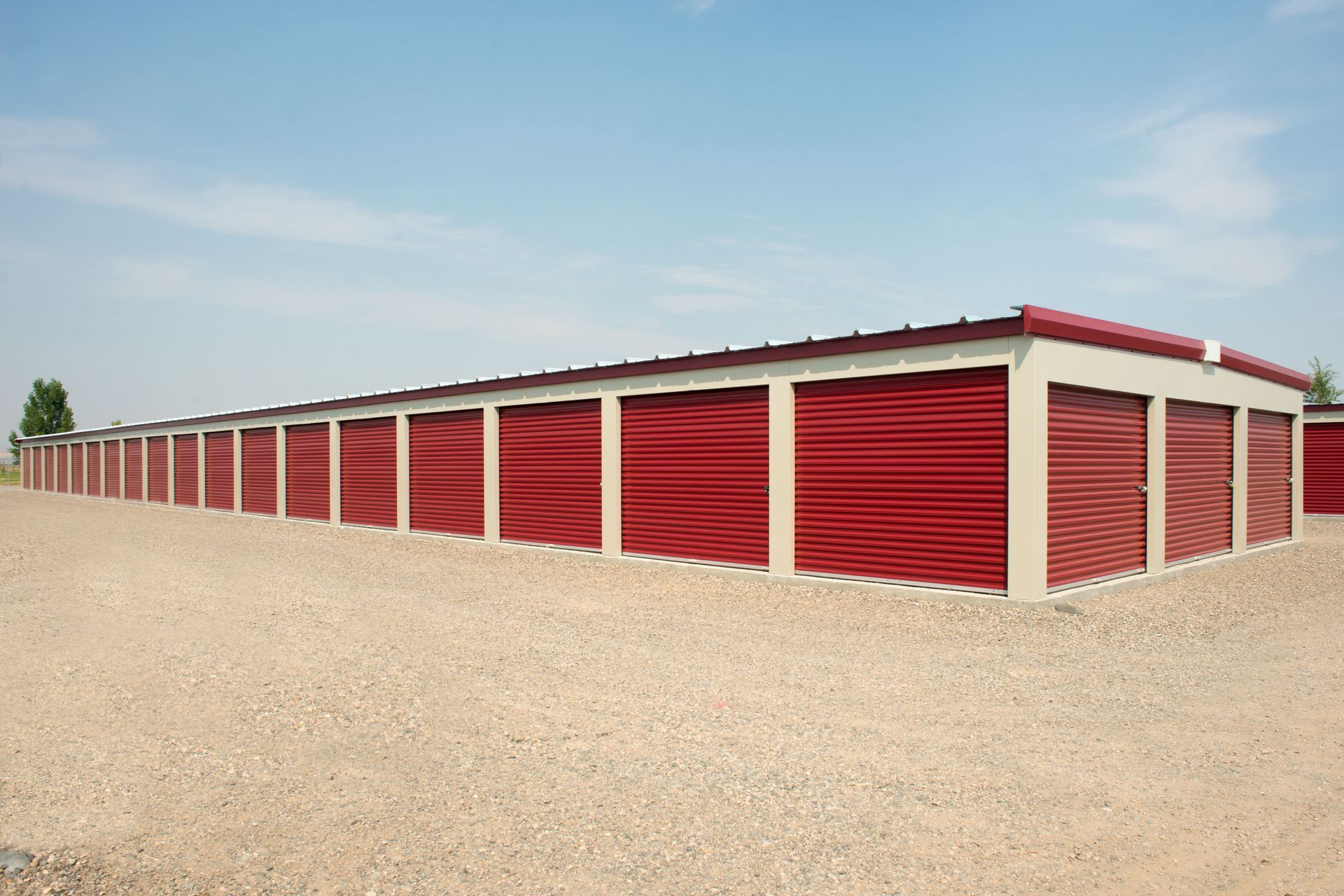 Red storage units in a row, under a blue sky. Gravel ground.
