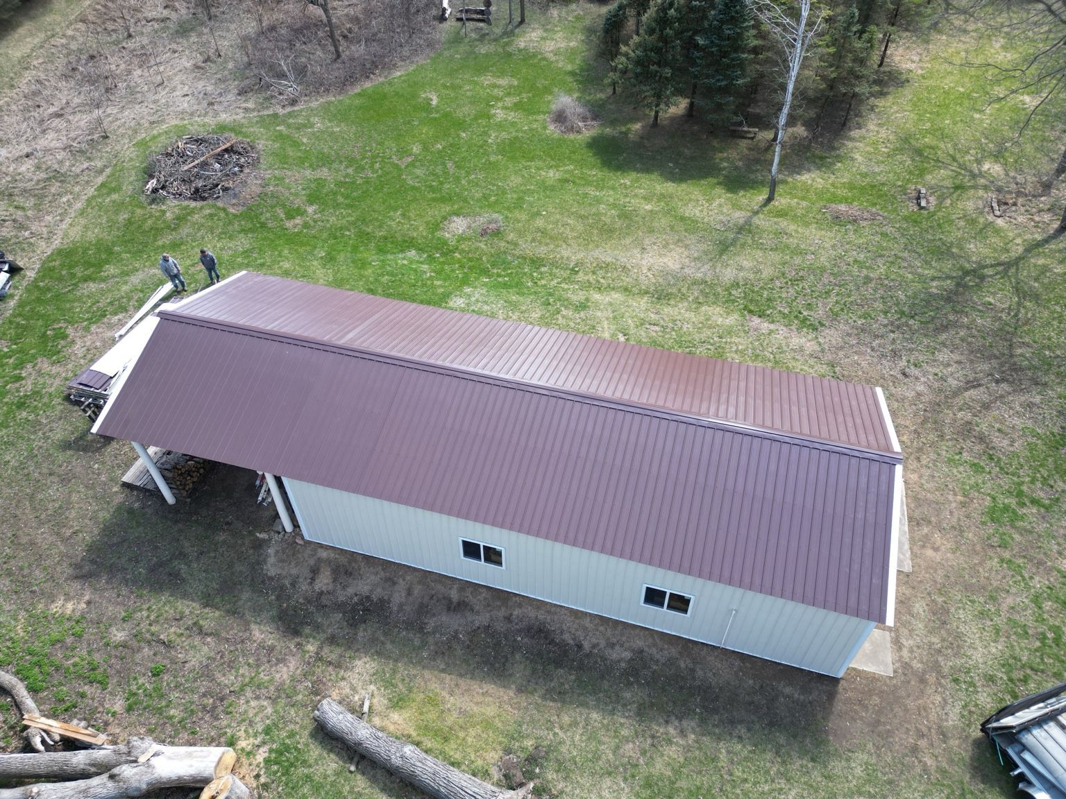Aerial view of a long white building with a brown metal roof in a grassy yard.