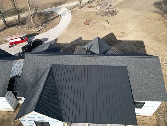 Aerial view of a house with a dark roof and a red truck parked on the driveway.