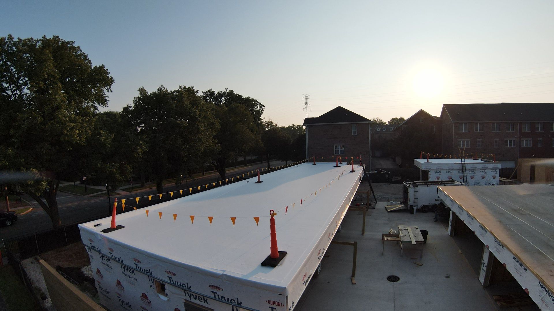 Rooftop at sunset with white canopy, orange cones, trees, and buildings in the background