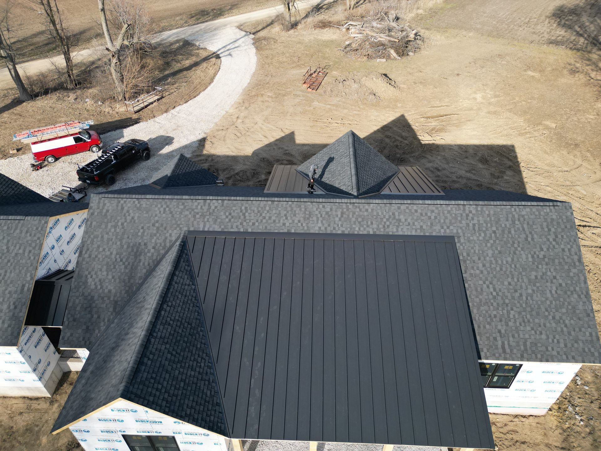 Aerial view of a house with a dark roof and curved driveway, with a red truck parked nearby.