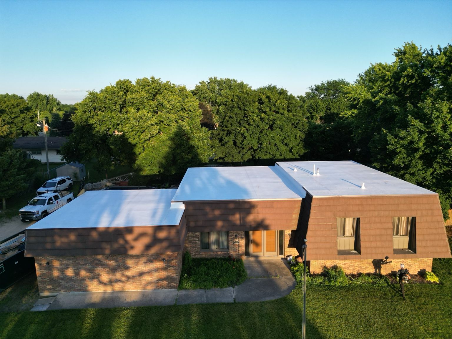 Aerial view of a brick house with white roofs, surrounded by green trees and lawn.