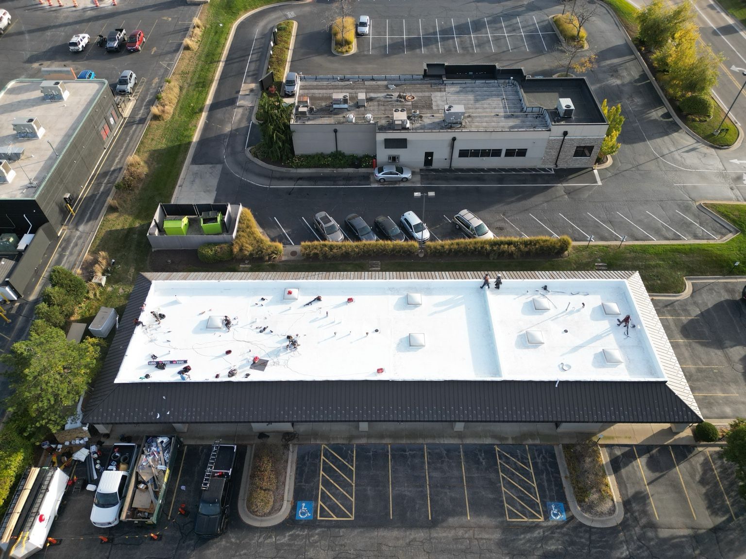 Aerial view of a white-roofed building, parking lots, and cars in an industrial area