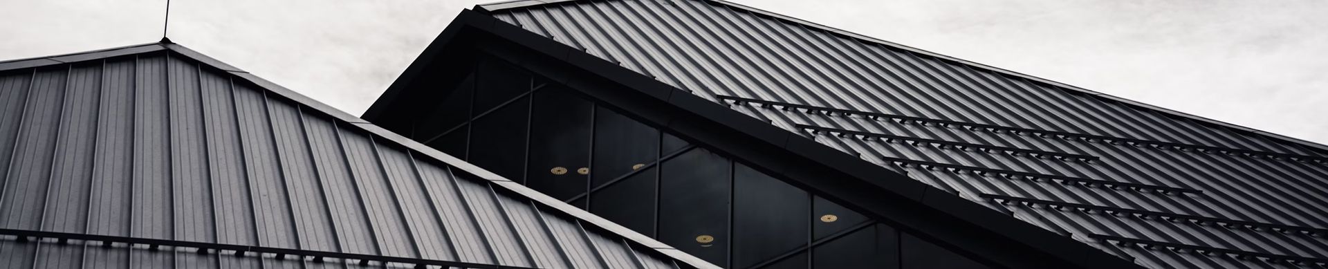 Close-up of two dark metal-roofed building sections with one light gray roof in the foreground