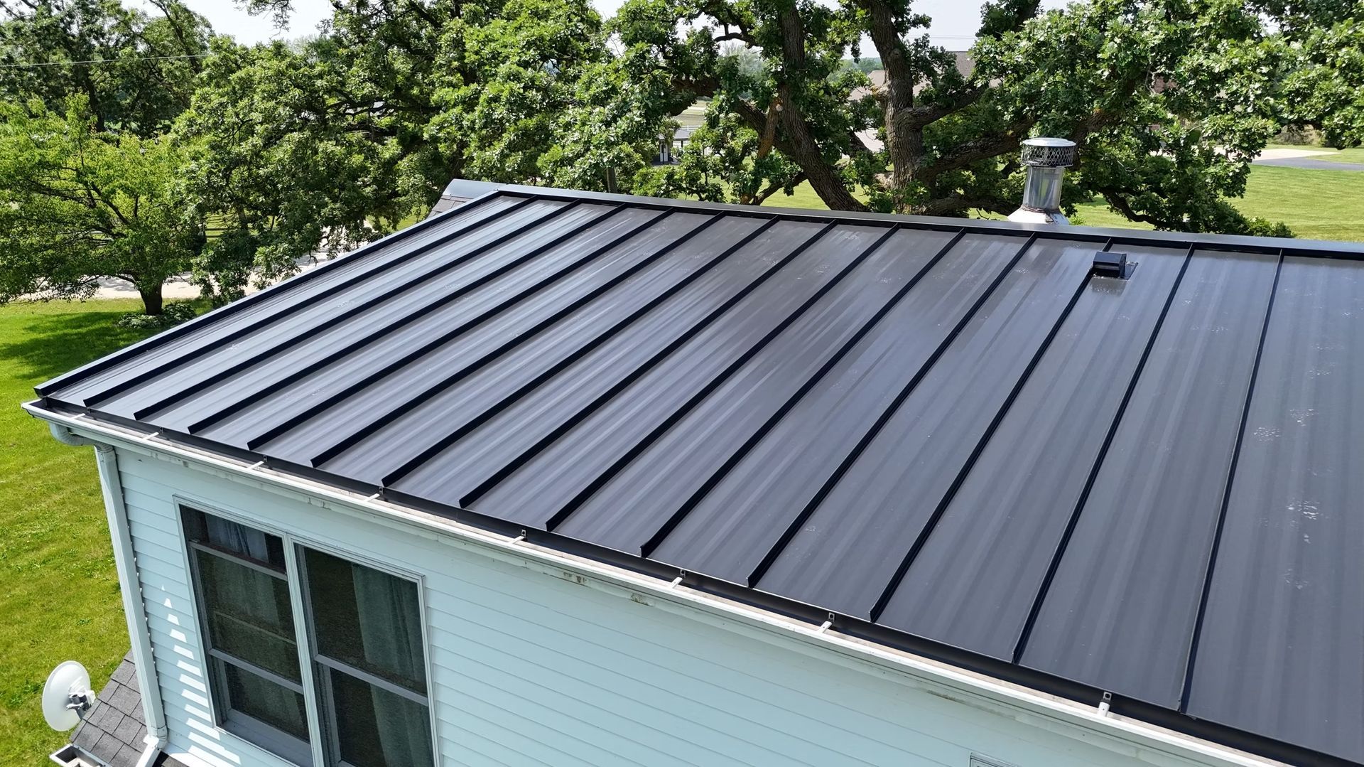 Black metal roof on a house with trees and green lawn in the background