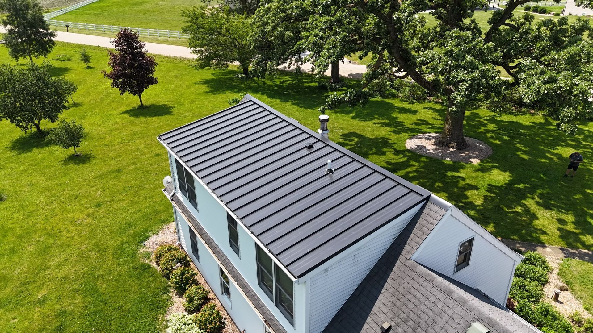 Aerial view of a modern house with a dark roof beside a green park and trees