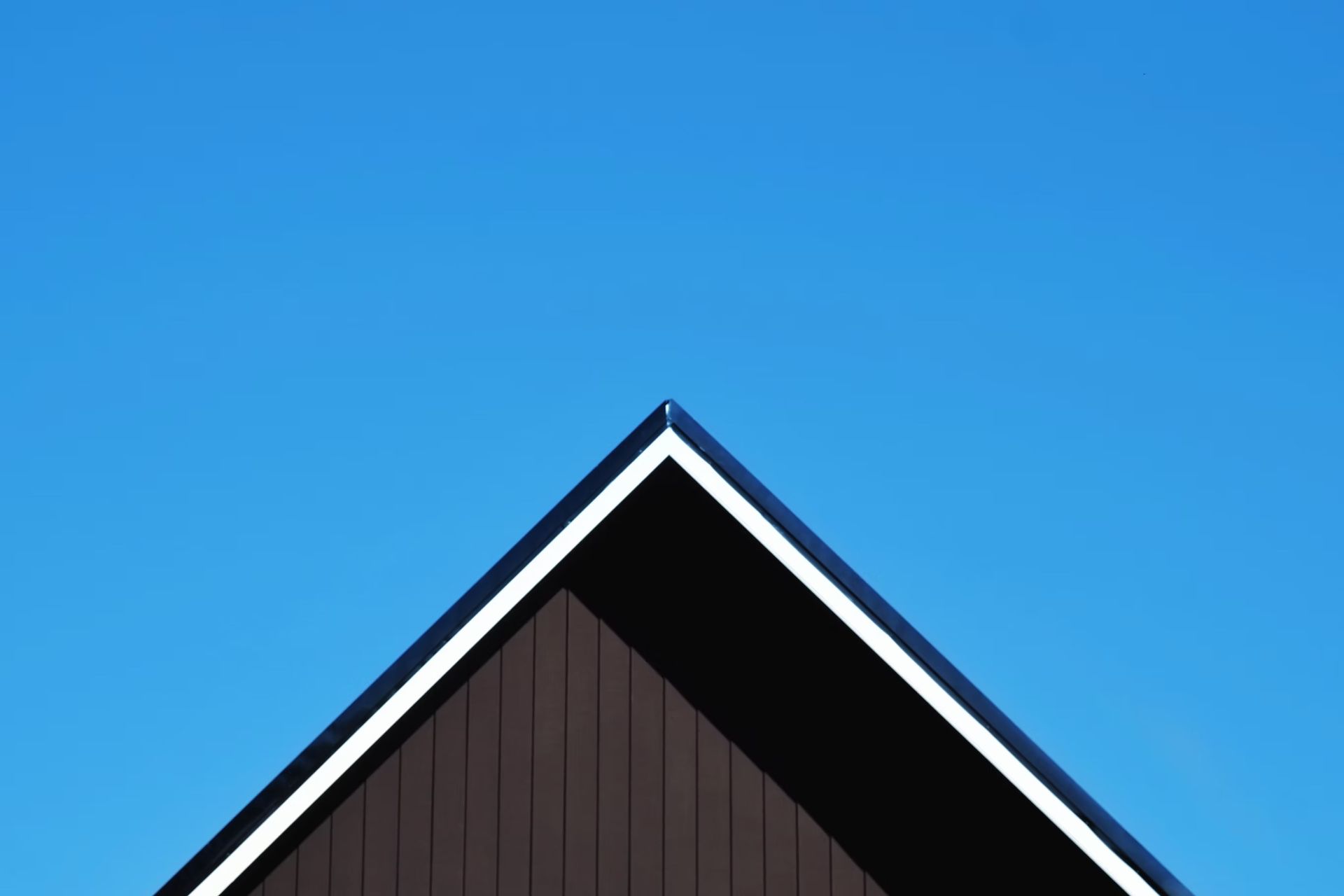 A dark house gable roof with white trim against a clear blue sky