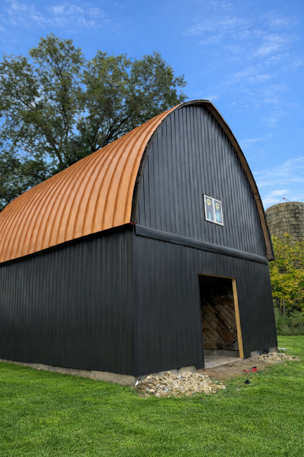 Black barn with orange arched roof and open doorway in a grassy field under blue sky