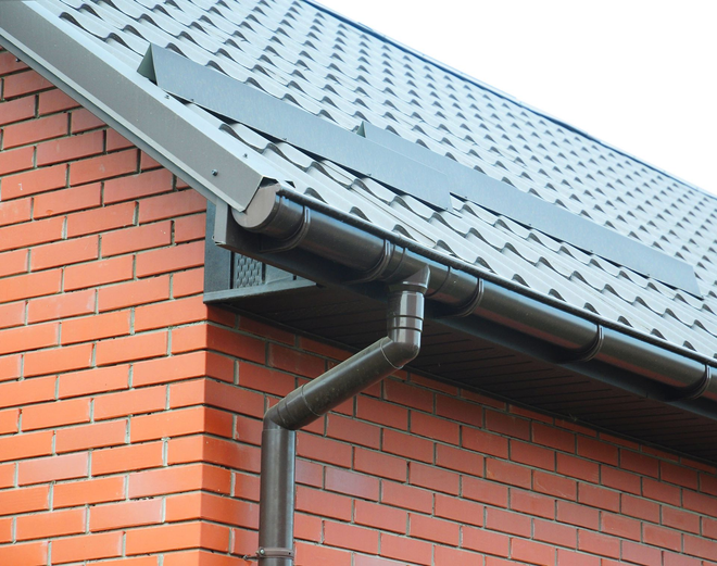 Gutter and downspout on a brick house with a gray metal roof