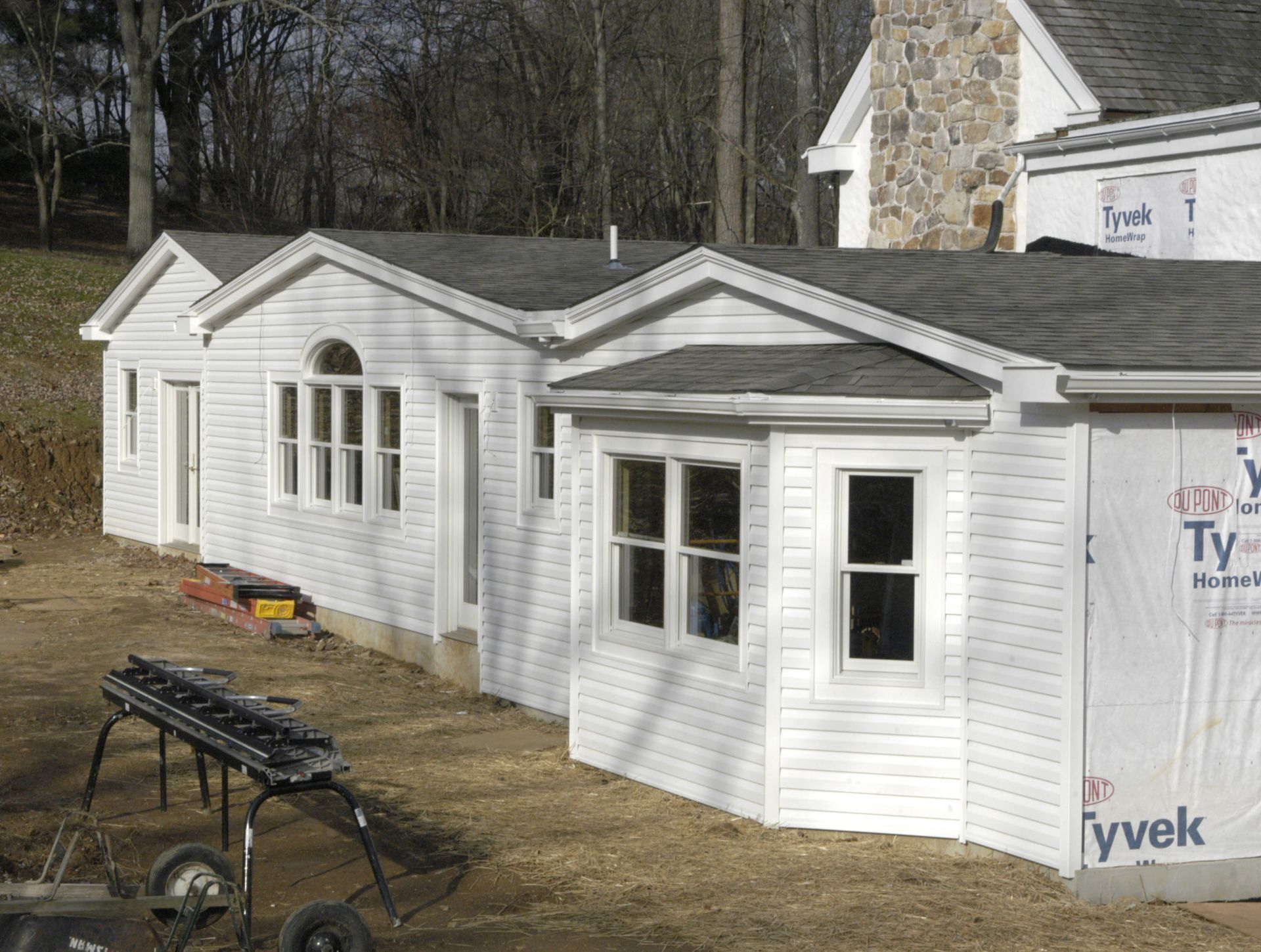 White house under construction with Tyvek wrap and exposed framing in a wooded area