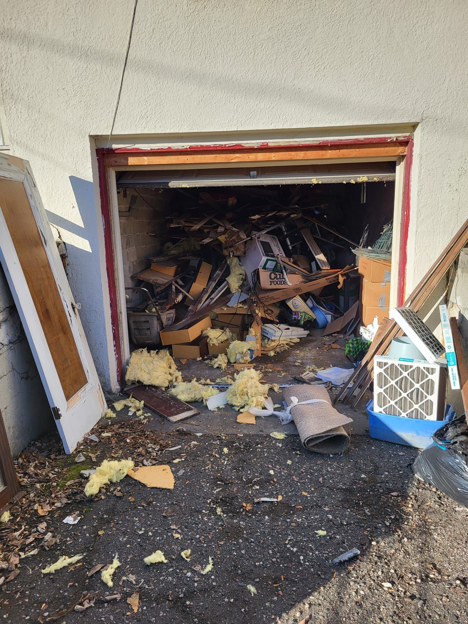 Garage doorway filled with debris; yellow insulation, wood, and other trash.