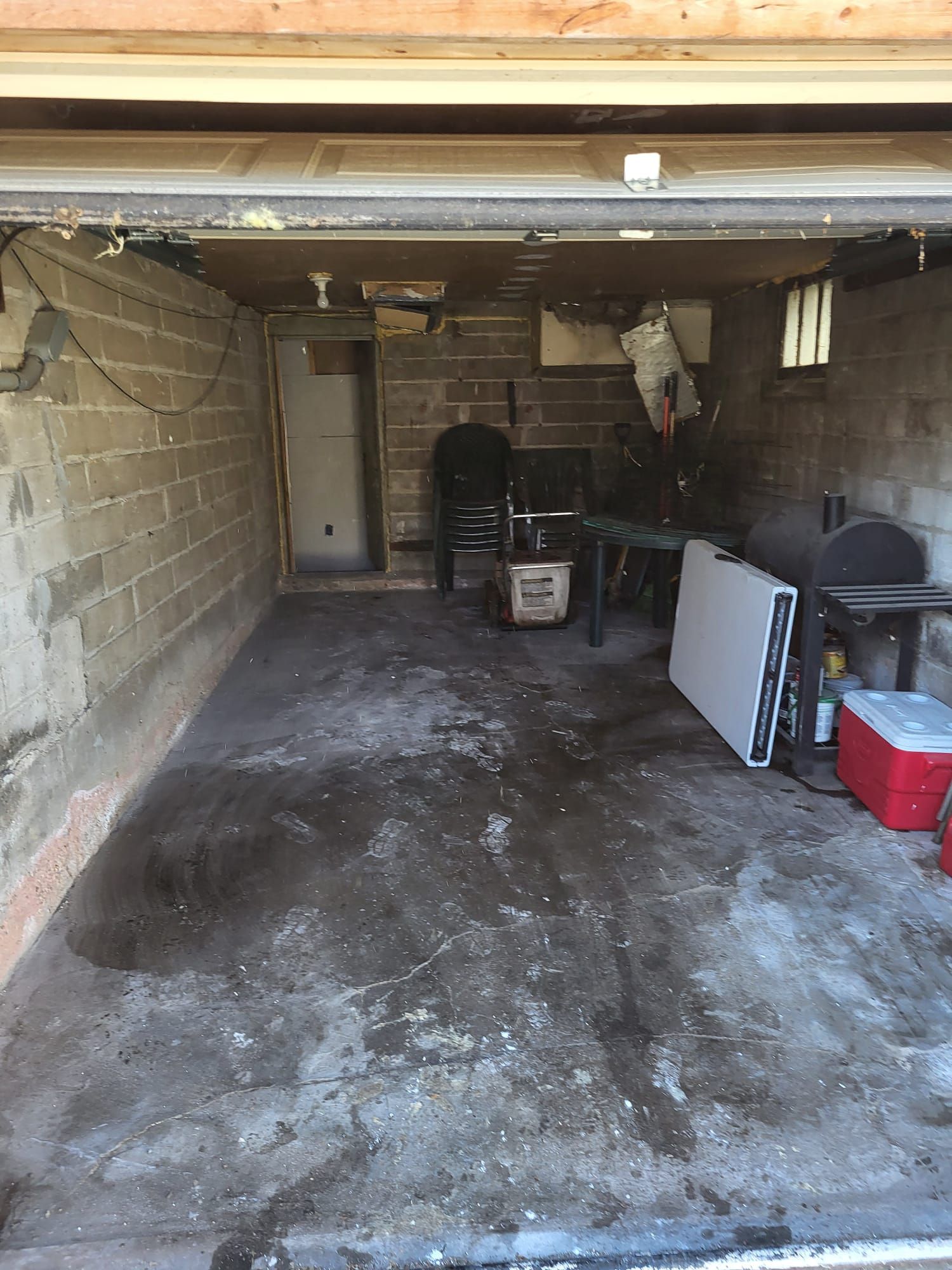 Interior of a garage with concrete floor and cinder block walls; a door and a table are visible.