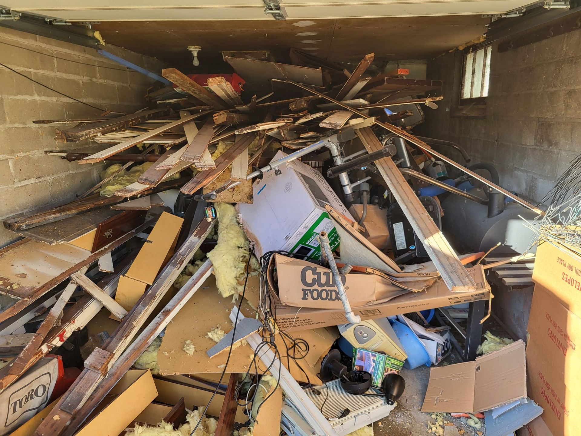 Pile of debris and junk fills a garage. Wood, cardboard, insulation, and other materials are visible.