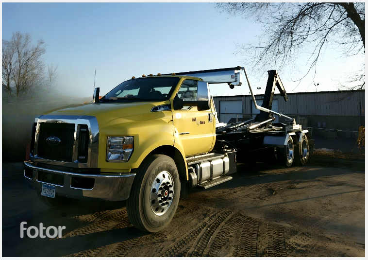 Yellow Ford truck with a roll-off container in an outdoor setting.
