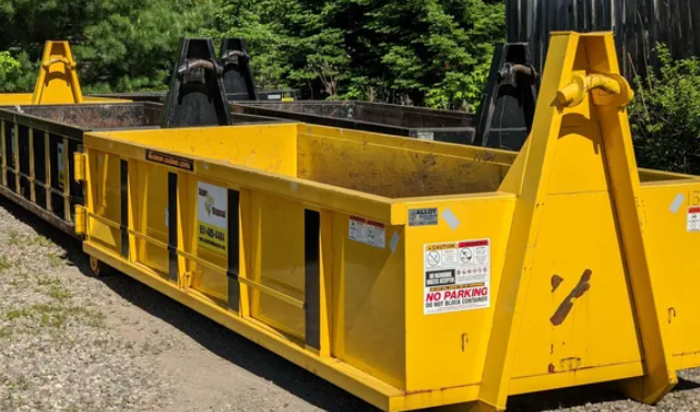 Yellow industrial dumpster with black lifting arms, outdoors.