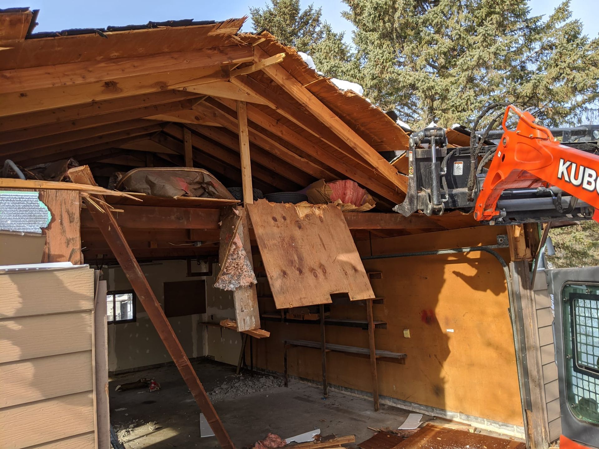 Orange Kubota machine demolishing a building's roof; sunny day.