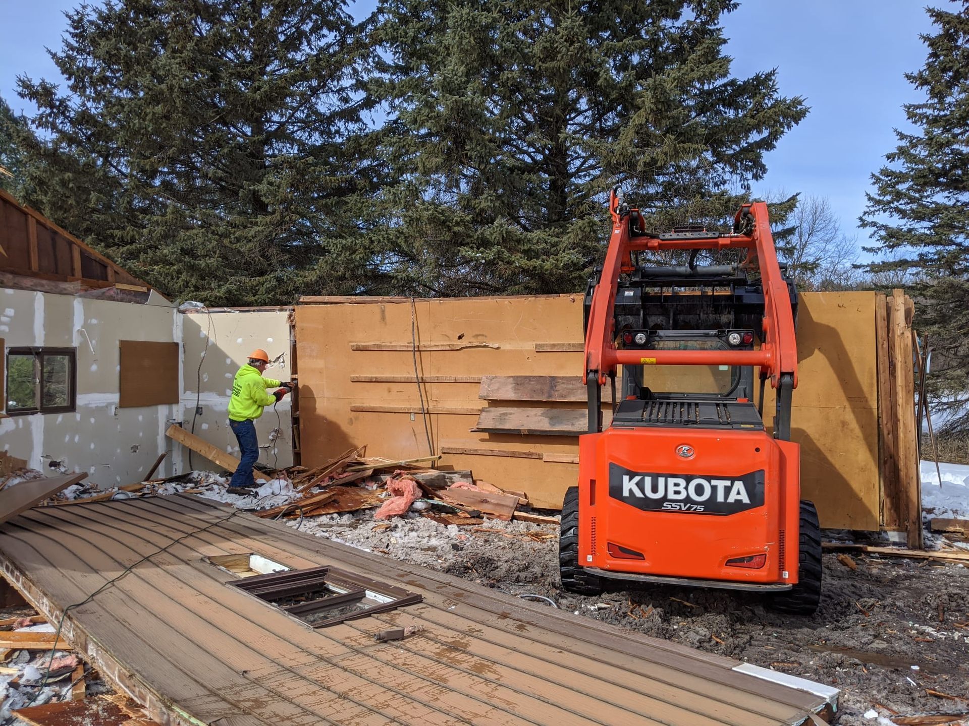 Construction worker in yellow vest uses Kubota skid steer to demolish a building.