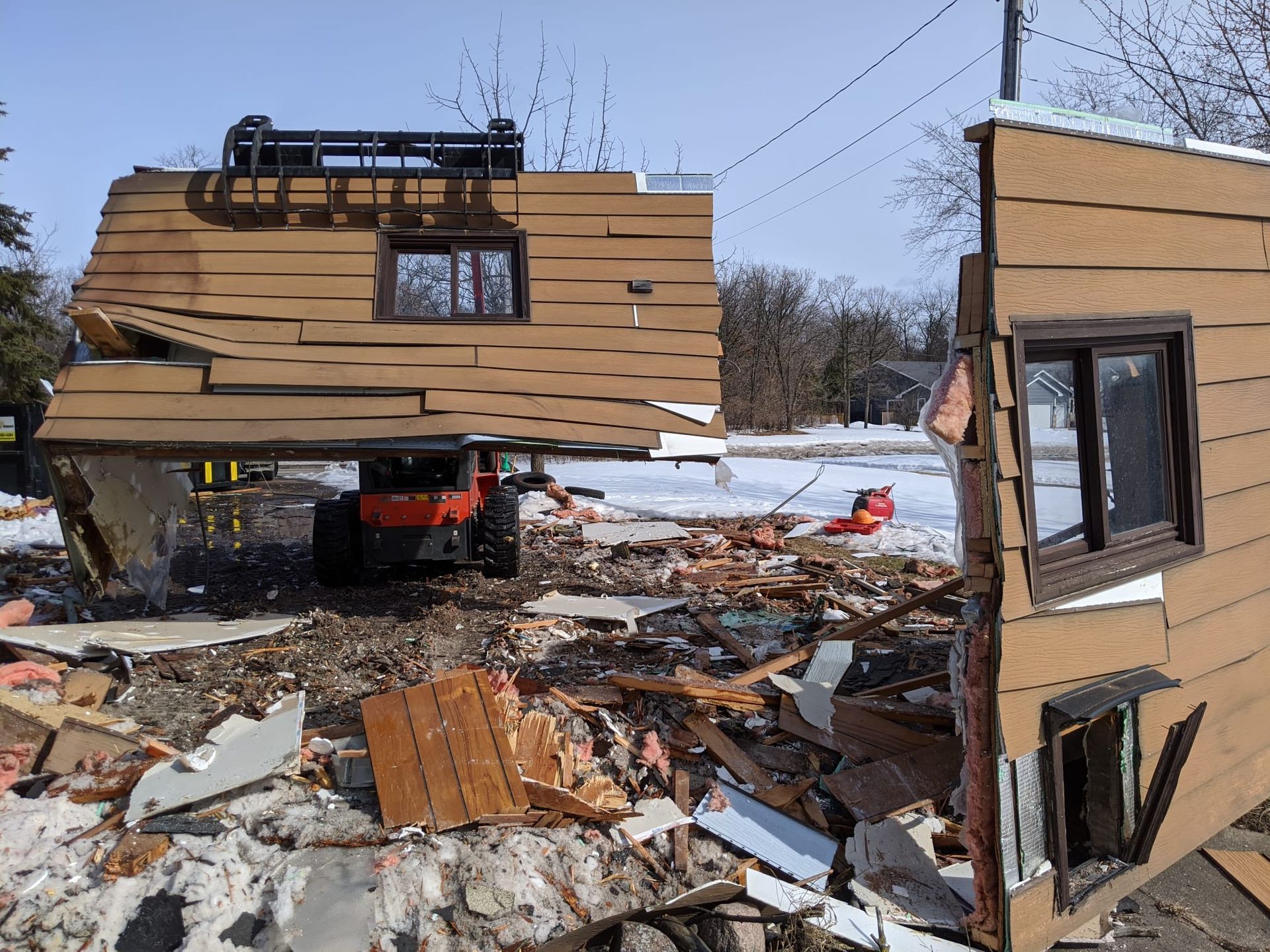 House demolition: A tractor carries a section of siding; debris litters the yard.