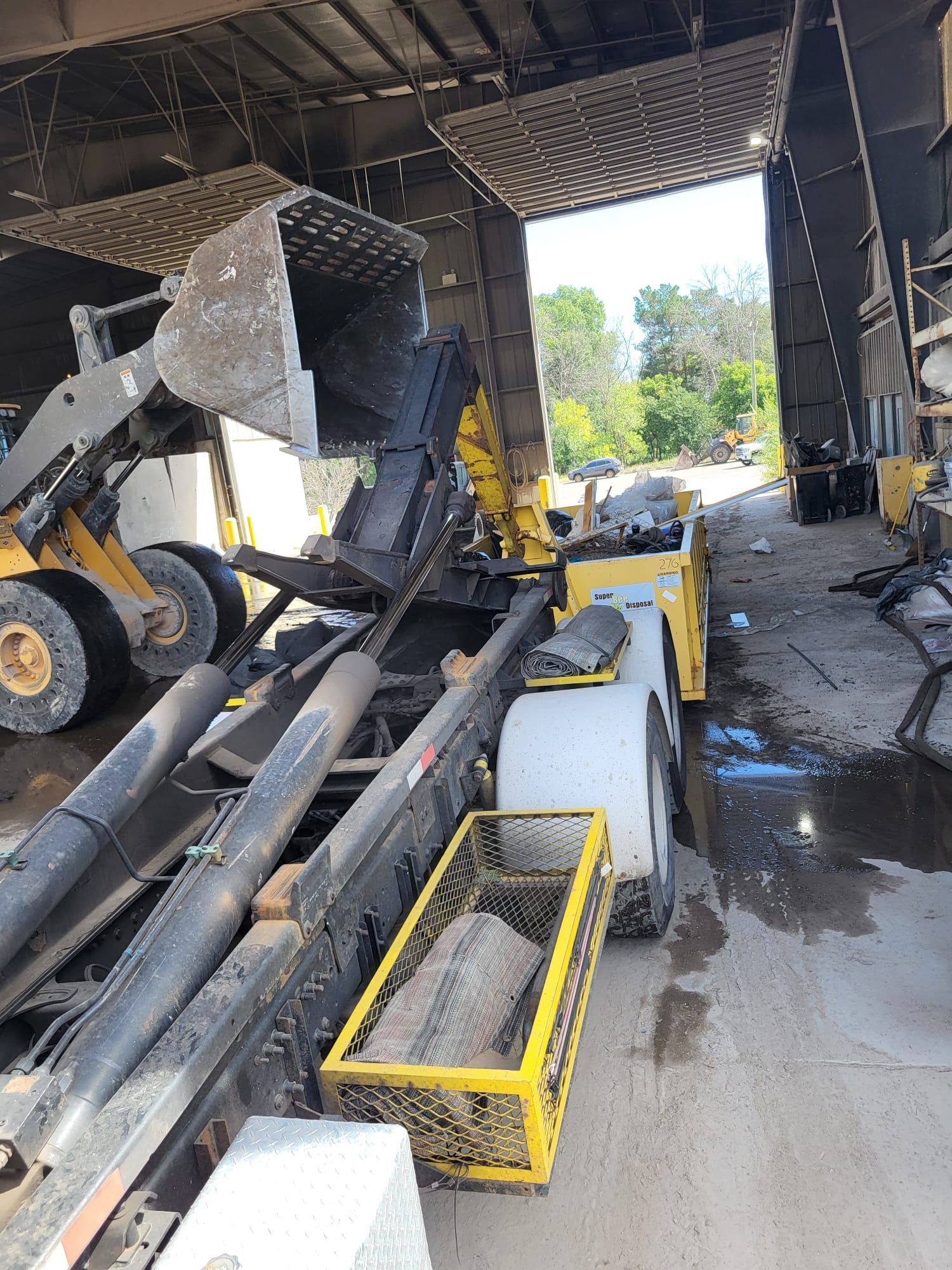 Yellow loader dumping material into a yellow trailer at a facility, likely for recycling.