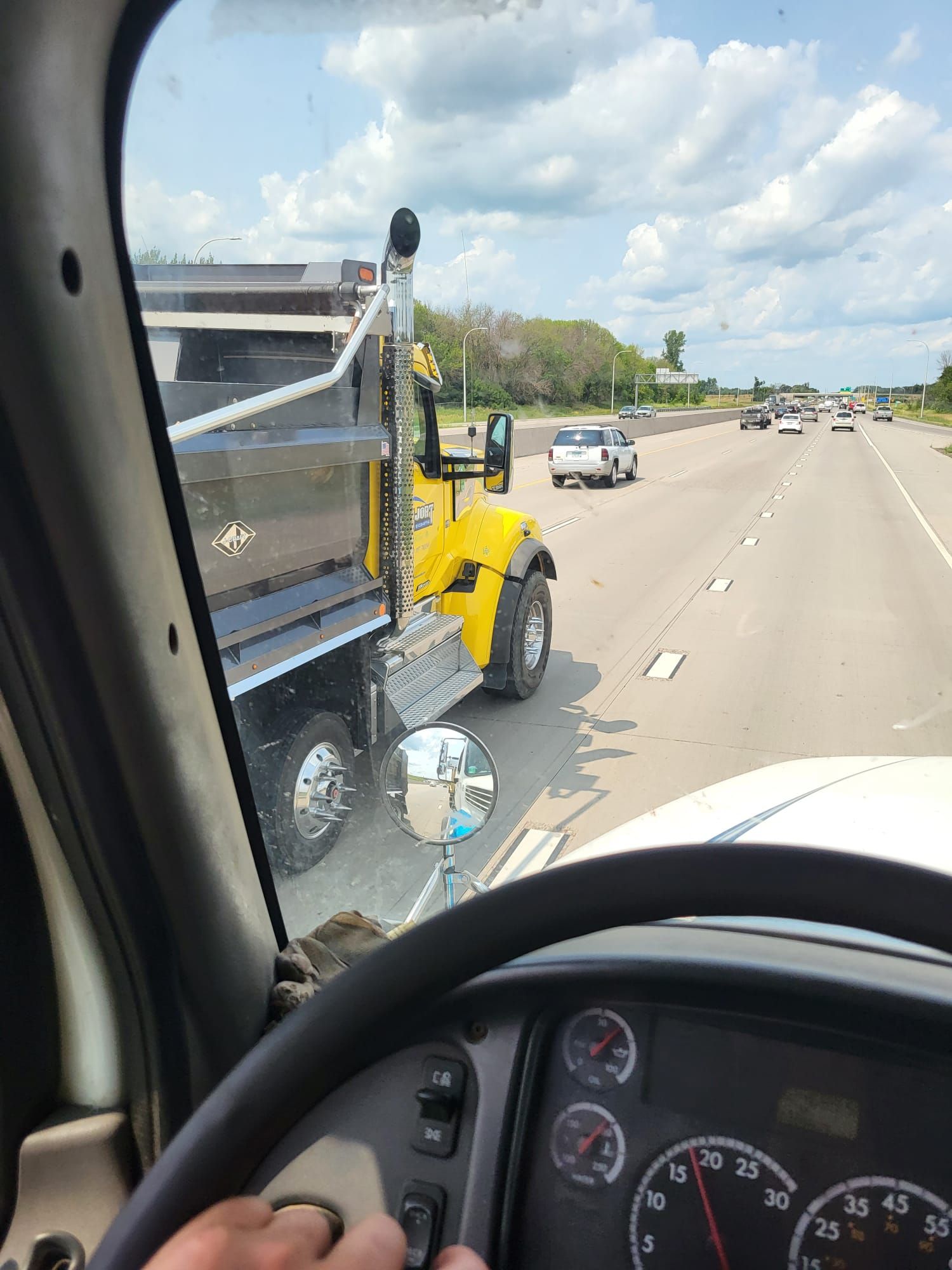 Yellow dump truck on a highway, viewed from inside another vehicle; cloudy sky.