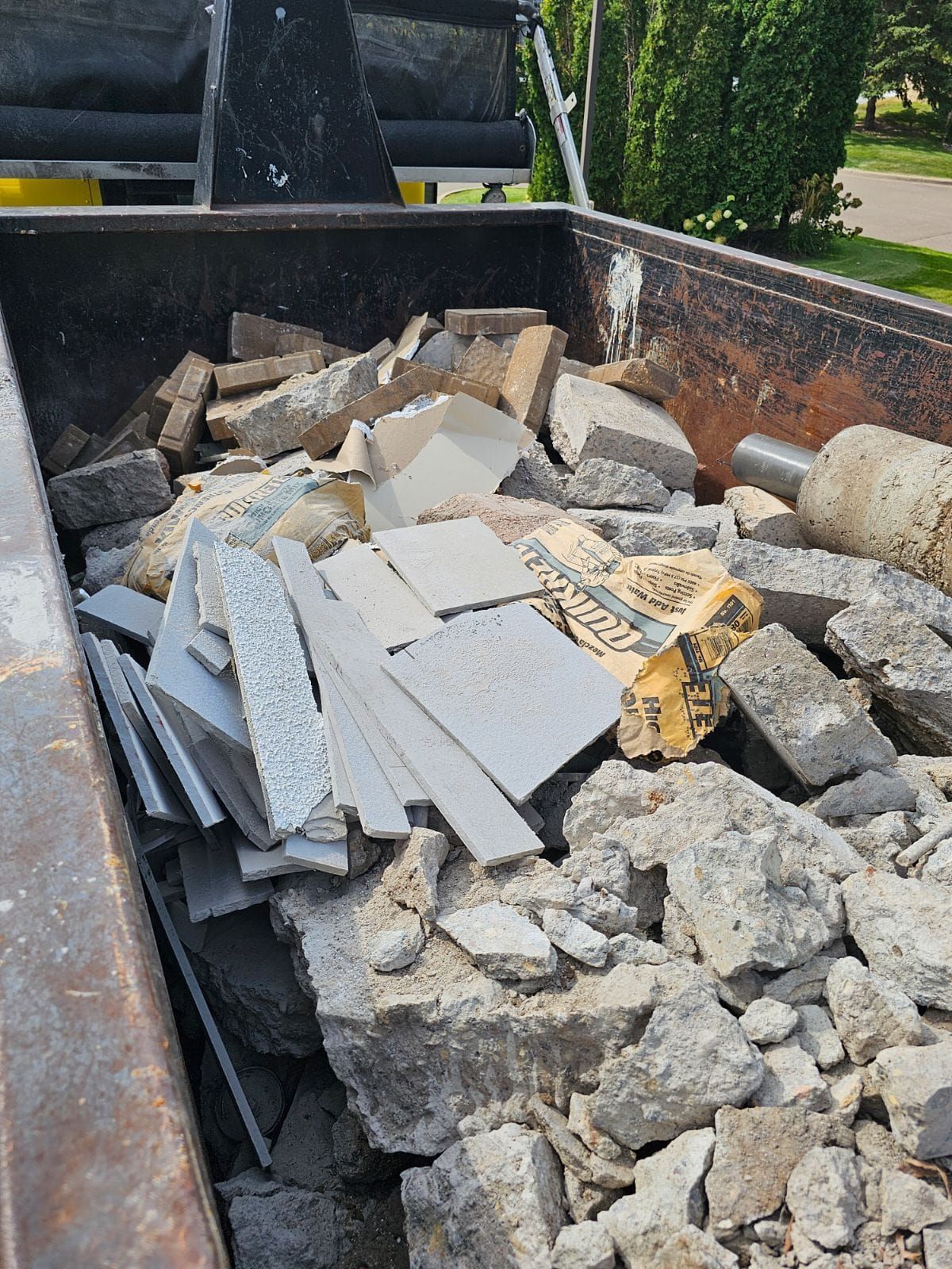 A dumpster filled with broken concrete, tiles, and debris.
