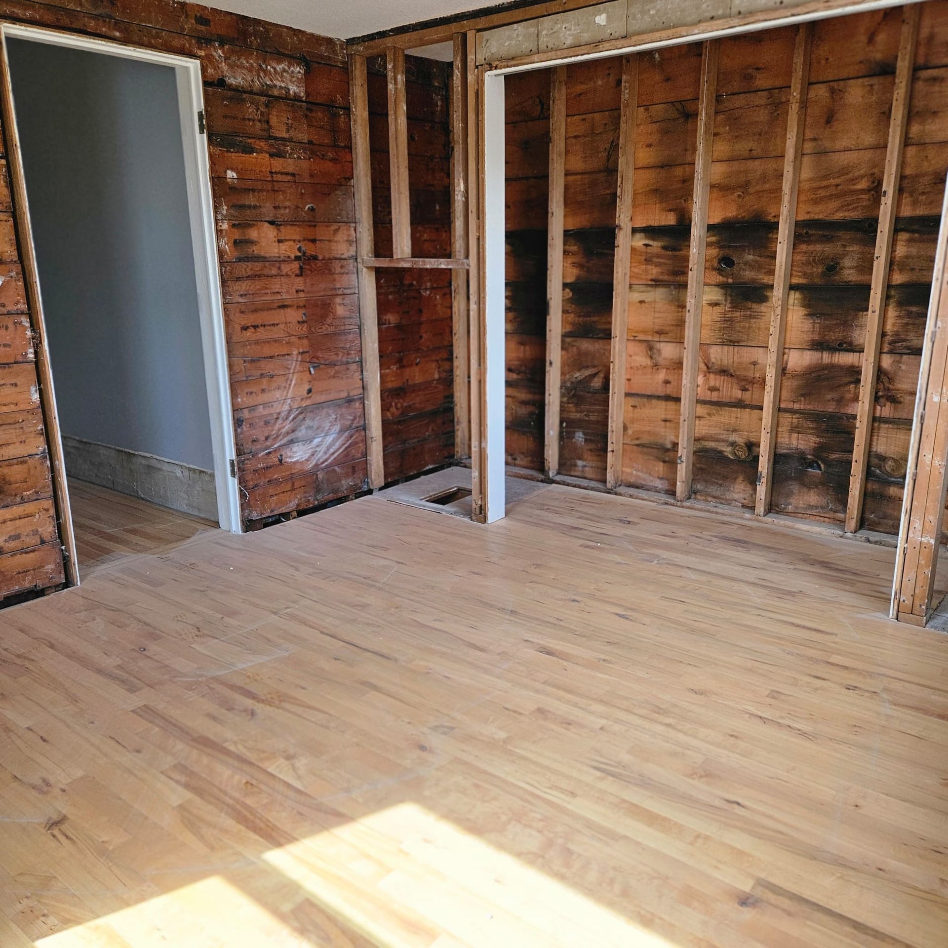 Room with hardwood floor and exposed wood walls; door frame on left, closet on right.