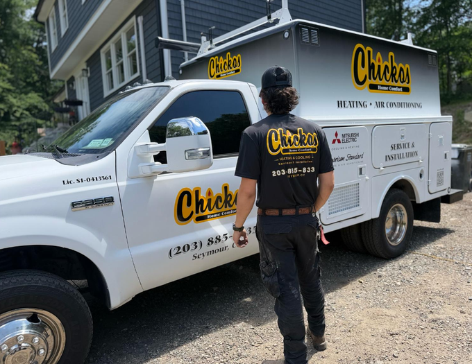 Worker standing by a white service truck in a driveway under bright sunlight