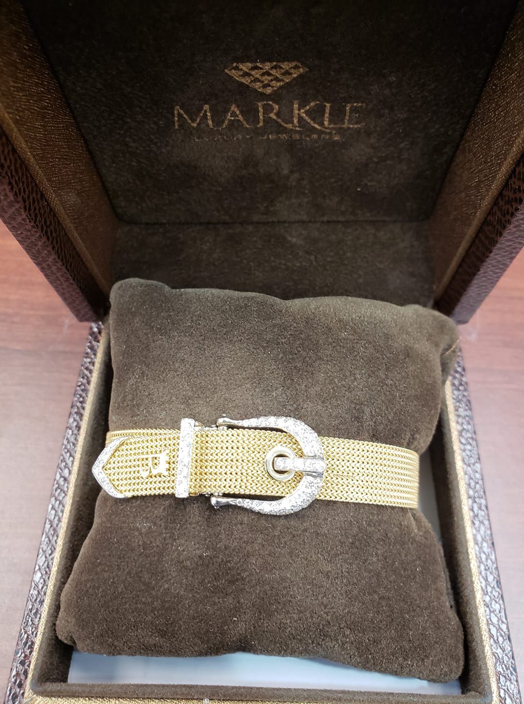 A gold bracelet is in a brown markle box
