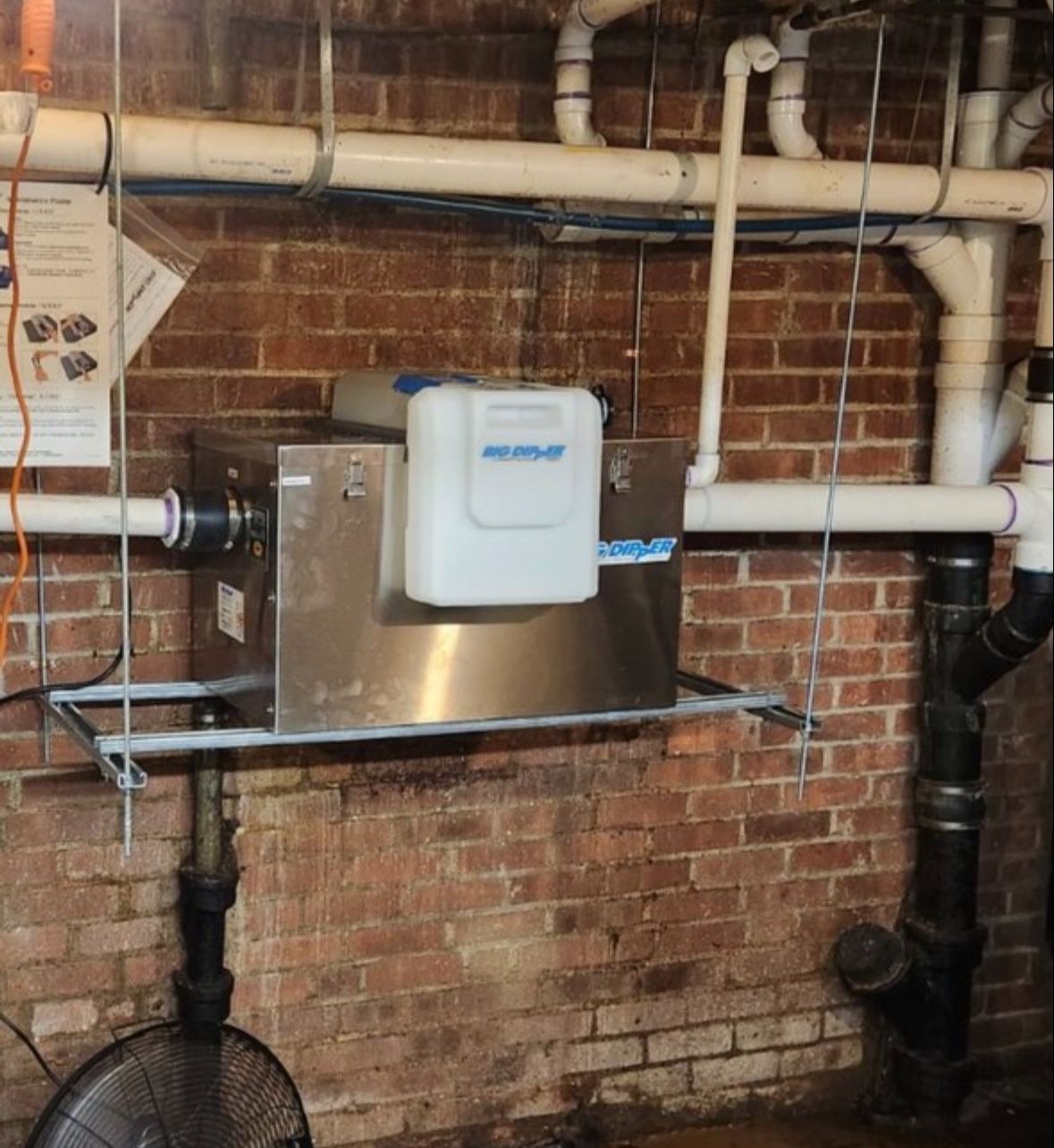 A brick wall with a fan and a stainless steel container