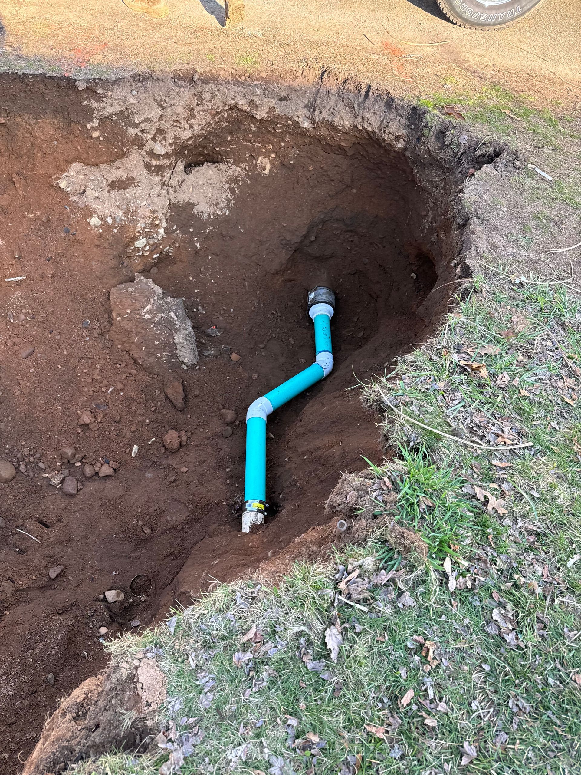 A blue pipe is laying in the dirt in a hole.