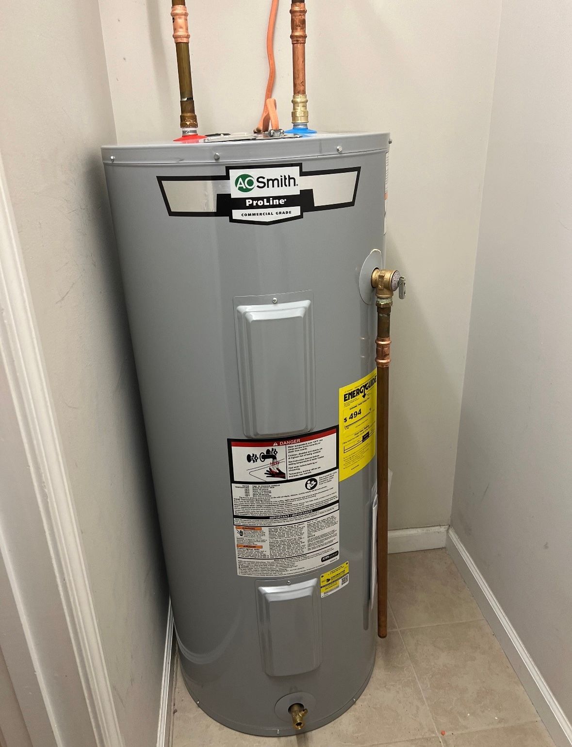 A gray water heater is sitting in a corner of a room.