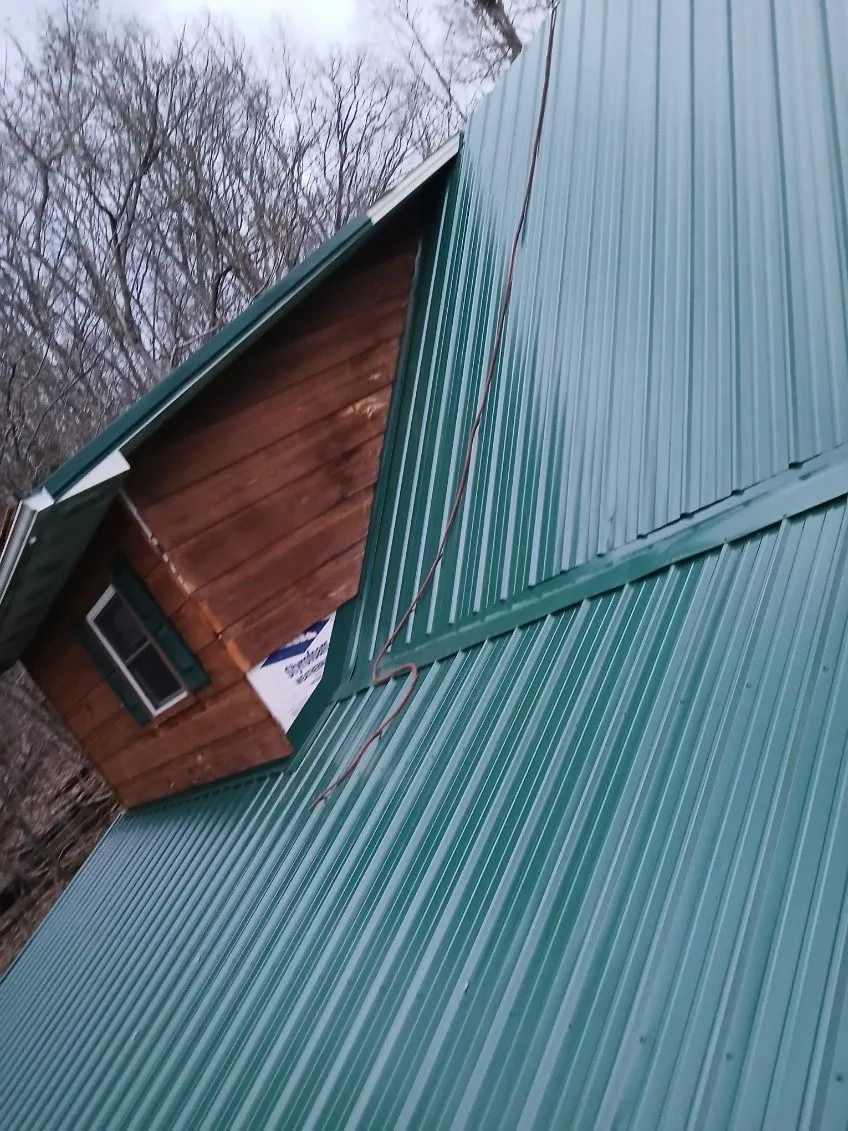 A green metal roof meets a wooden dormer wall with an exposed, unfinished gap near the window.