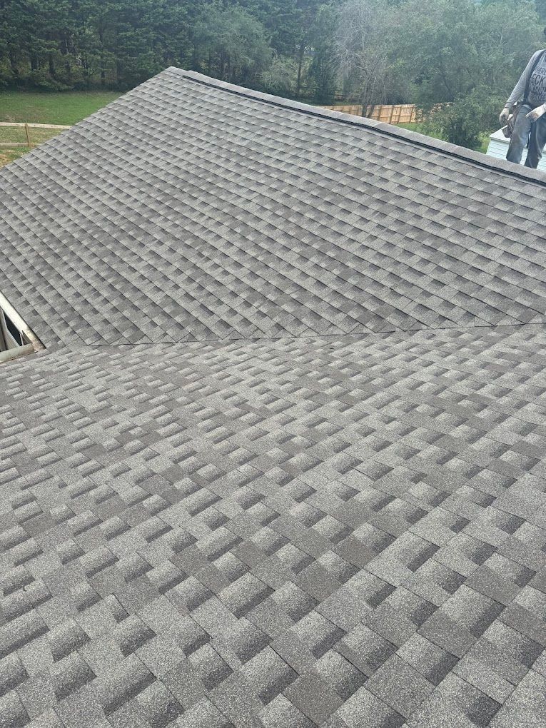 A gray shingled roof under construction with a person standing on the right edge.